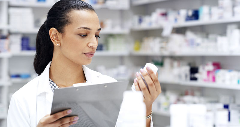 female pharmacist in pharmacy holding a digital tablet inspecting a pill bottle