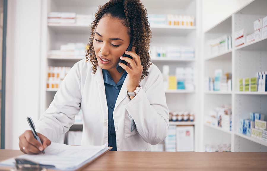 Female pharmacist talking on cellphone and writing on clipboard